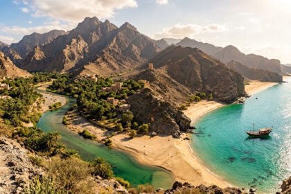 Dramatic coastal landscape in Oman featuring rugged mountains, turquoise waters, sandy beaches and a traditional dhow boat.