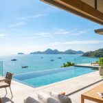 Modern luxury villa terrace with an unobstructed panoramic ocean view under a clear blue sunny sky.