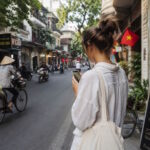 Woman using a smartphone on a busy street in Vietnam, illustrating everyday life for expats navigating the country without speaking Vietnamese.