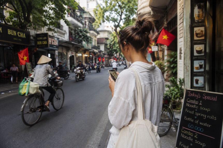 Woman using a smartphone on a busy street in Vietnam, illustrating everyday life for expats navigating the country without speaking Vietnamese.